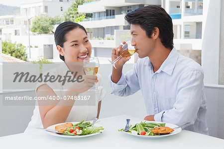 Happy couple having a meal together with white wine outside on a balcony