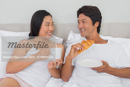 Happy couple having breakfast in bed at home in bedroom