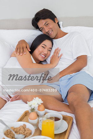 Happy couple having breakfast in bed at home in bedroom