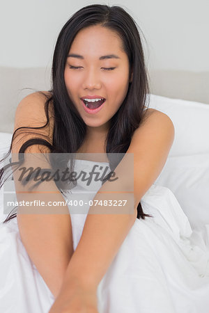 Smiling woman lying in bed yawning in the morning at home in bedroom