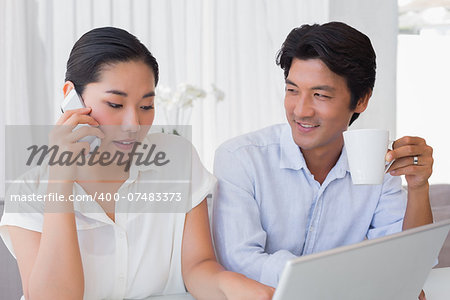 Couple using laptop with woman talking on phone at home in the living room