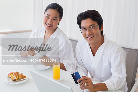 Couple in bathrobes shopping online in the morning at home in the living room
