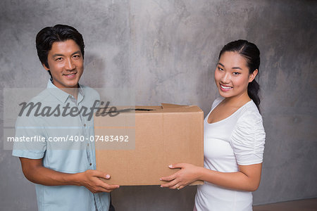 Happy couple holding a cardboard moving box in their new home