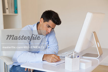 Casual businessman writing at his desk in his office