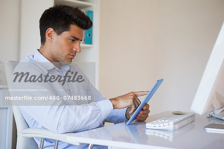 Casual businessman working on his tablet at his desk in his office