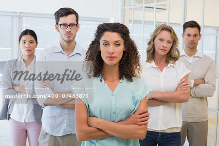 Casual business team frowning at camera with arms crossed in the office