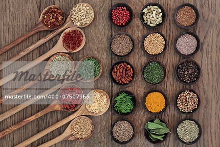 Herb and spice food seasoning selection in wooden spoons and bowls over oak wood background.