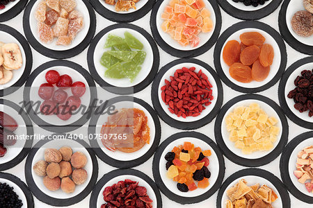 Dried fruit selection in white bowls on slate rounds over white background.