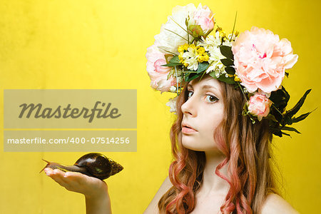 calm pretty girl with snail in hand and flower crown on head on yellow background
