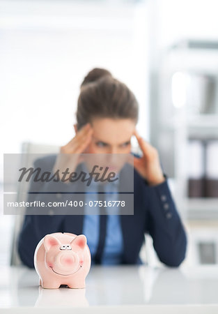 Closeup on piggy bank and stressed business woman in background