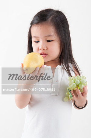 Child eats fruit. Little Asian girl eating pear and grapes, isolated on white background