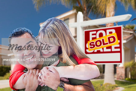 Happy Hugging Mixed Race Couple in Front of Sold Home For Sale Real Estate Sign and House.