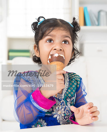 Eating ice cream. Cute Indian Asian girl enjoying an ice cream. Beautiful child model at home.