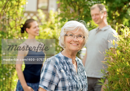 Senior woman smiling in front of two young people, outdoors