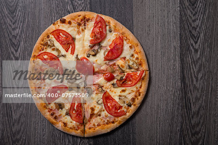 High angle view of delicious Italian pizza with ham and tomatoes on gray wooden table