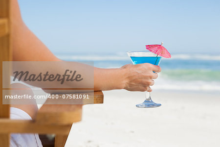 Woman sitting in deck chair with a cocktail at the beach on a sunny day