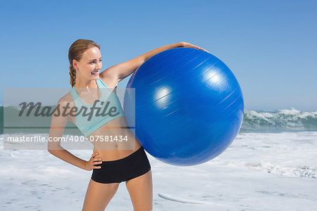 Fit woman standing on the beach holding exercise ball on a sunny day