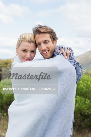 Cute smiling couple standing outside wrapped in blanket on a chilly day