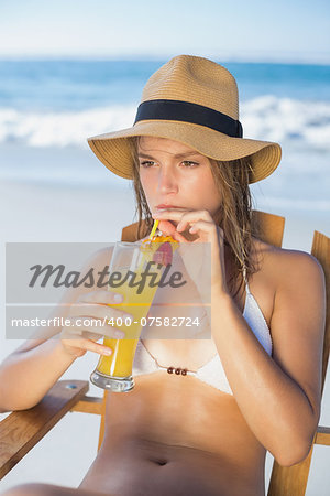 Pretty blonde relaxing in deck chair on the beach with cocktail on a sunny day