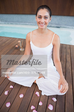 Peaceful brunette in white sitting in lotus pose surrounded by petals in health spa
