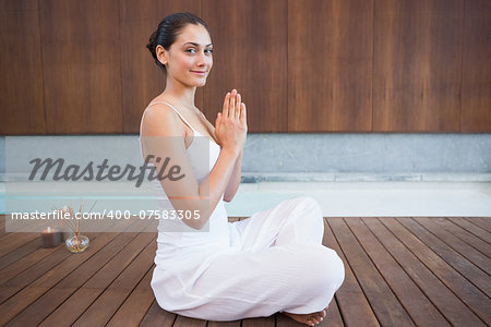 Content brunette in white sitting in lotus pose smiling at camera in health spa