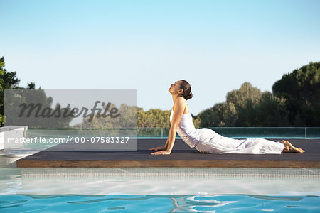 Peaceful brunette in cobra pose poolside on a sunny day at the spa
