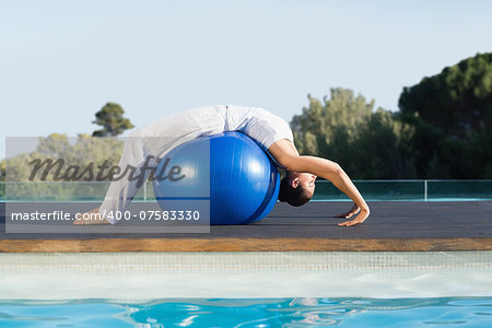 Peaceful brunette in cobra pose over exercise ball poolside on a sunny day at the spa
