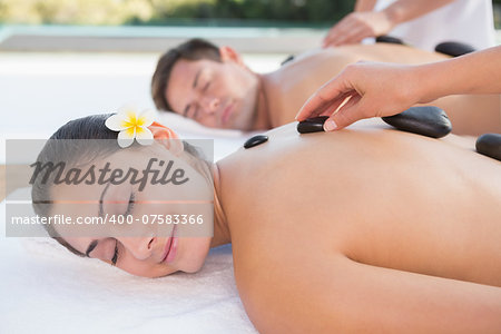 Attractive couple enjoying hot stone massage poolside outside at the spa