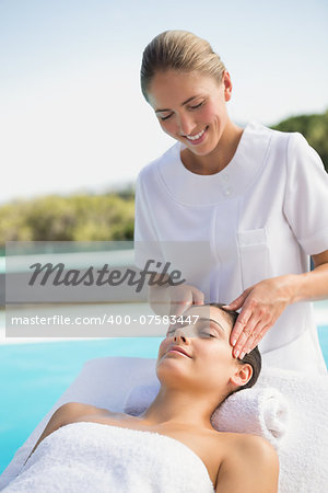 Tranquil brunette getting a head massage poolside outside at the spa