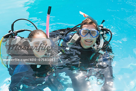 Smiling couple on scuba training in swimming pool looking at camera on a sunny day