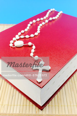 Holy rosary beads with a crucifix on top of a Christian Bible.