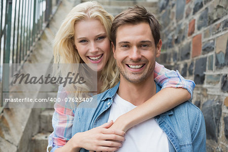 Hip young couple sitting on steps smiling at camera on a sunny day in the city
