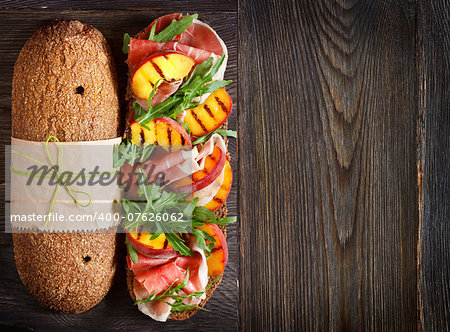 Delicious ham sandwich with grilled peaches and arugula on an wooden background with place for text.