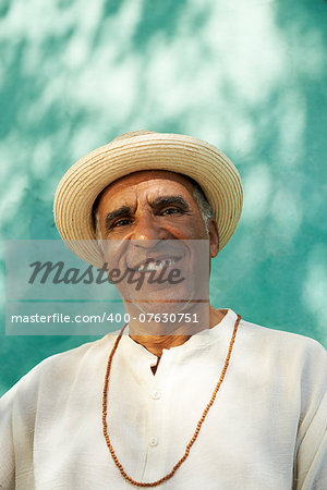 Portrait of retired senior hispanic man with straw hat sitting in park and looking at camera with happy expression