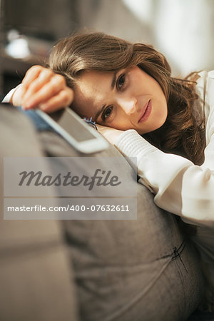 Concerned young woman with cell phone sitting on couch