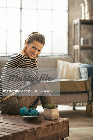 Smiling young woman sitting on coffee table in loft apartment