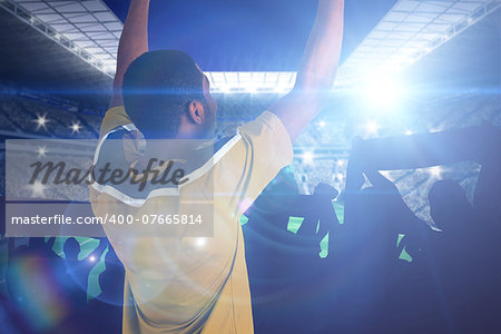 Cheering football fan in yellow jersey against large football stadium with lights