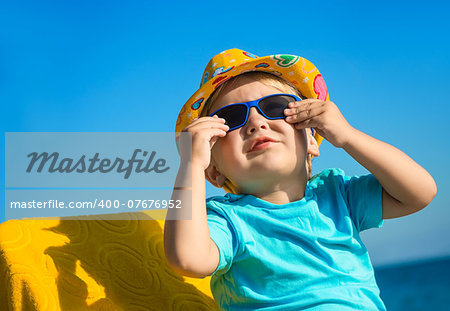 Boy kid in sun glasses and hat on beach against blue sky