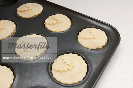 Mince pies in a bun tin ready for the oven, with pastry holly leaf decoration