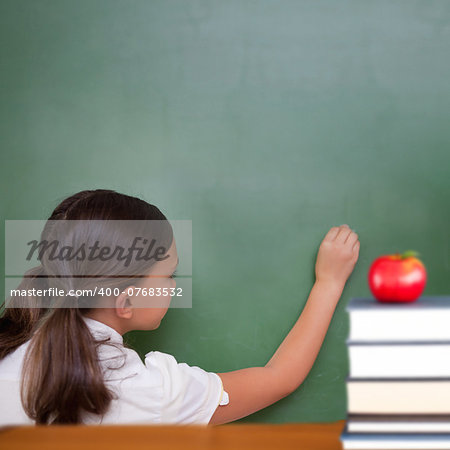 Red apple on pile of books against cute pupil writing on chalkboard