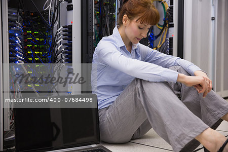 Stressed technician sitting on floor beside open server in large data center