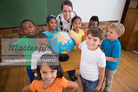 Cute pupils pointing to globe in classroom at the elementary school