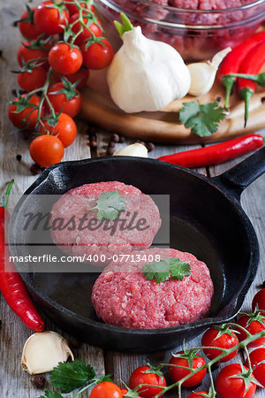 Raw meatballs on iron pan with chili pepper, cherry tomato and garlic. Selective focus.