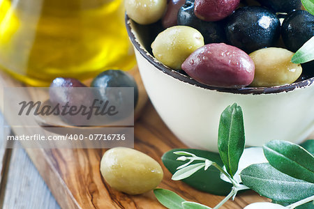Mixed marinated olives (green, black and purple) in ceramic bowl and wooden spoon with bottle of olive oil. Selective focus.