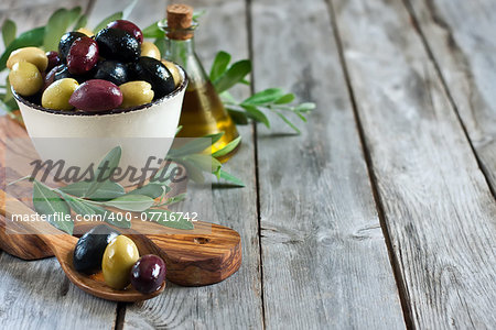 Mixed marinated olives (green, black and purple) in ceramic bowl and wooden spoon with bottle of olive oil. Selective focus. Copy space background