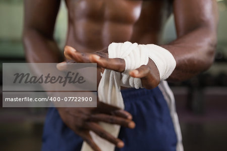Close-up mid section of a shirtless muscular man binds bandage on his hand