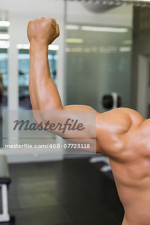 Close-up rear view of a shirtless muscular man flexing muscles in gym