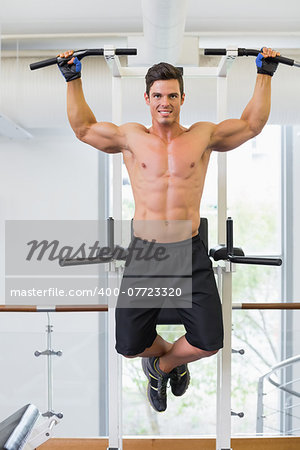 Shirtless male body builder doing pull ups at the gym