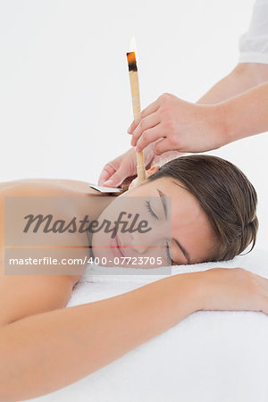 Side view of a beautiful young woman receiving ear candle treatment at spa center