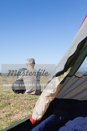 Happy camper sitting outside his tent holding sleeping bag on a sunny day